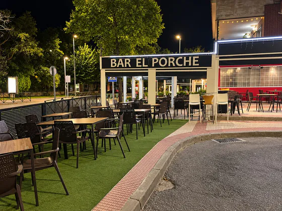 Terraza de Bar El Porche de noche, con mesas sobre césped y el rótulo iluminado