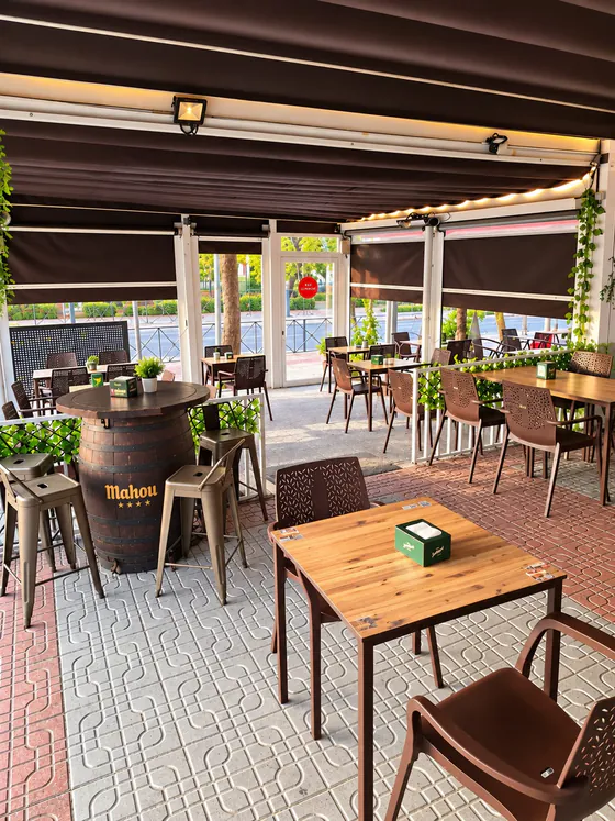 Terraza cubierta de El Porche con barril de Mahou, taburetes y mesas de madera