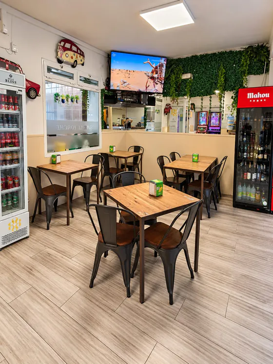 Comedor interior de El Porche con mesas de madera, plantas y televisión